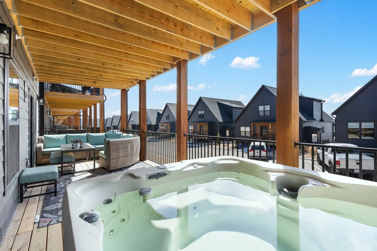 The image showcases the exterior of a spacious single-family home with rustic wooden beams, an inviting hot tub, and a comfortable outdoor seating area on a large deck. The scene is set during golden hour, highlighting panoramic sunset views over Table Rock Lake. The atmosphere is tranquil and welcoming, perfect for gatherings and relaxation.