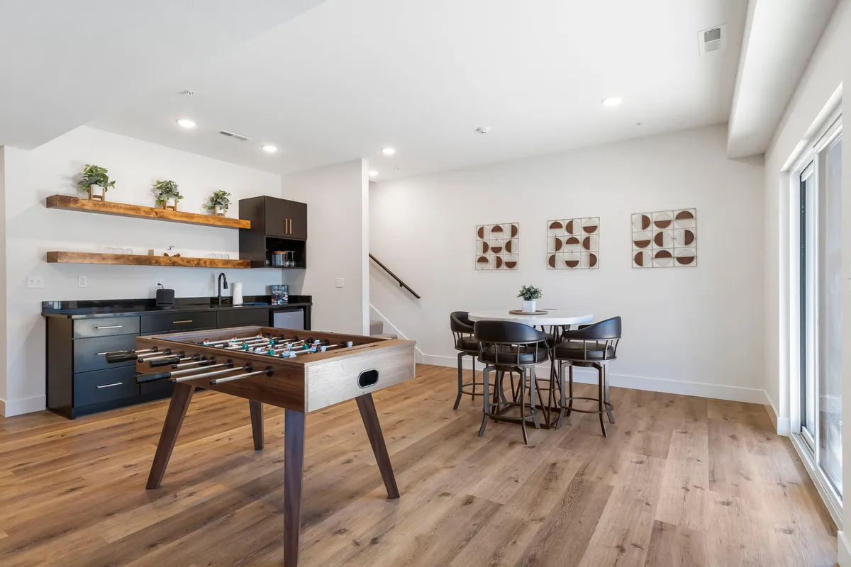A vibrant game room featuring a foosball table and a dining table set against open shelving and decorative wall art. The space exudes a playful and social vibe, perfect for gatherings, with plenty of room for friendly competitions and relaxed meals.