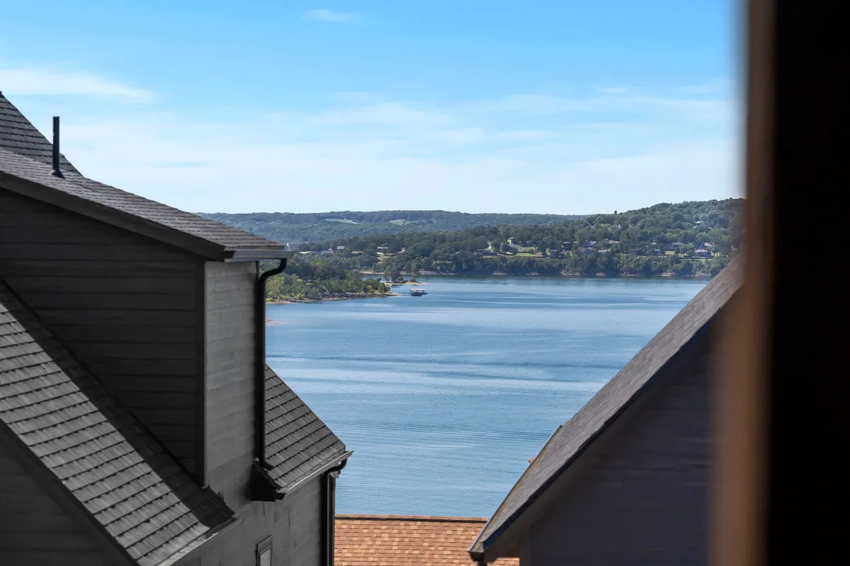 A tranquil lake view captures the expansive waters of Table Rock Lake with distant shores and rooftops in the foreground. The serene setting invites activities like boating, fishing, or simply relaxing by the water, underscoring the property's close proximity to the lake.