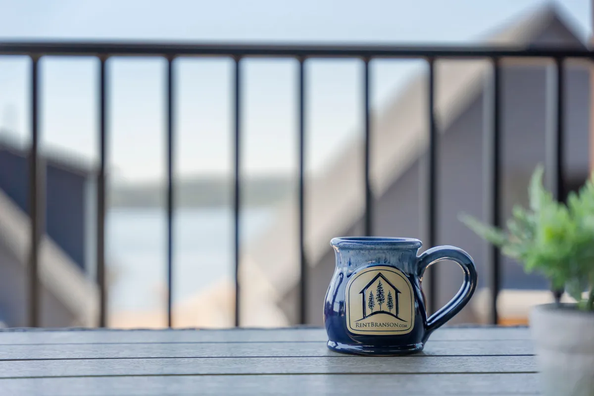 A serene balcony scene with a ceramic mug perched on the railing, overlooking a distant water view. The tranquil setting suggests a peaceful morning ritual, such as sipping coffee while taking in the natural beauty.