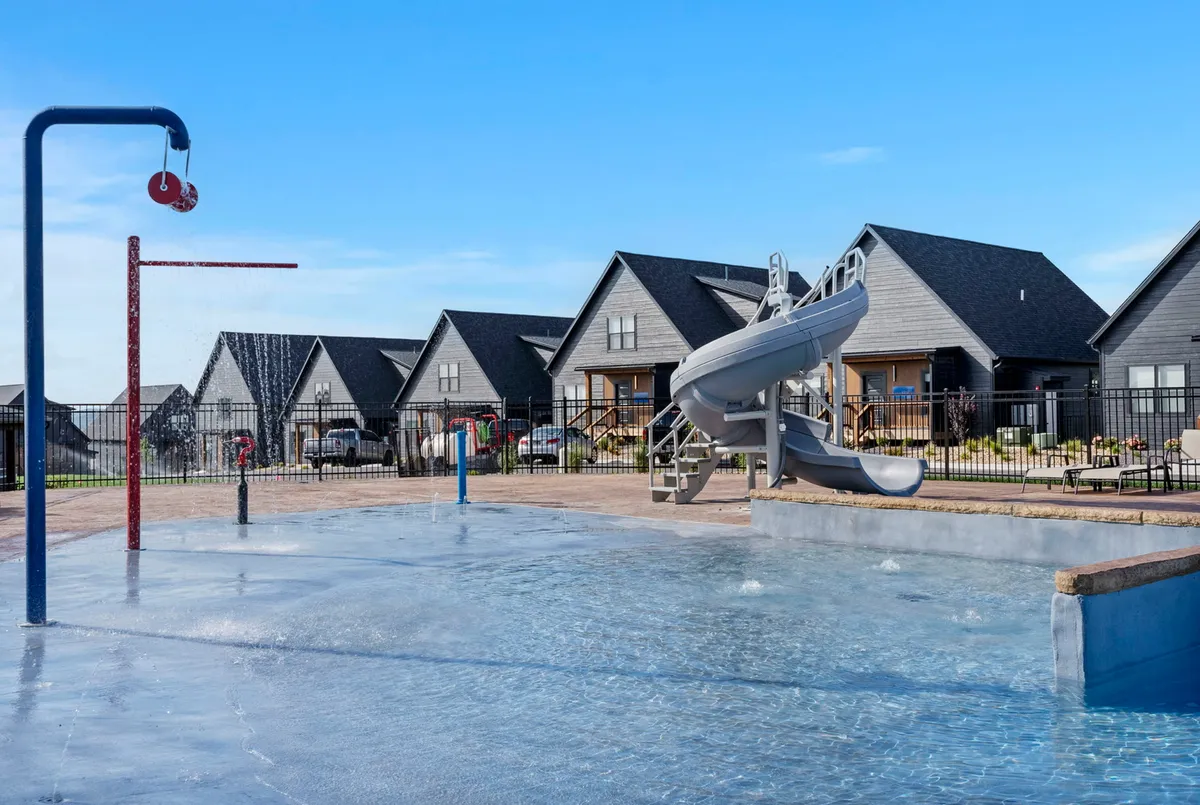 A vibrant swimming pool scene surrounded by houses, featuring a playful water slide and spray features. Families and friends gather by the pool to swim, play, and relax, capturing the essence of summer fun and community events.