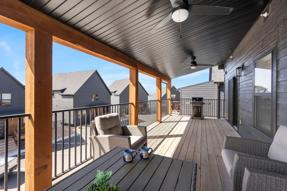 An inviting outdoor deck with a comfortable seating area, grill, and wooden railings, set up for al fresco dining or relaxing. The space looks out over the natural surroundings, hinting at the lake beyond.