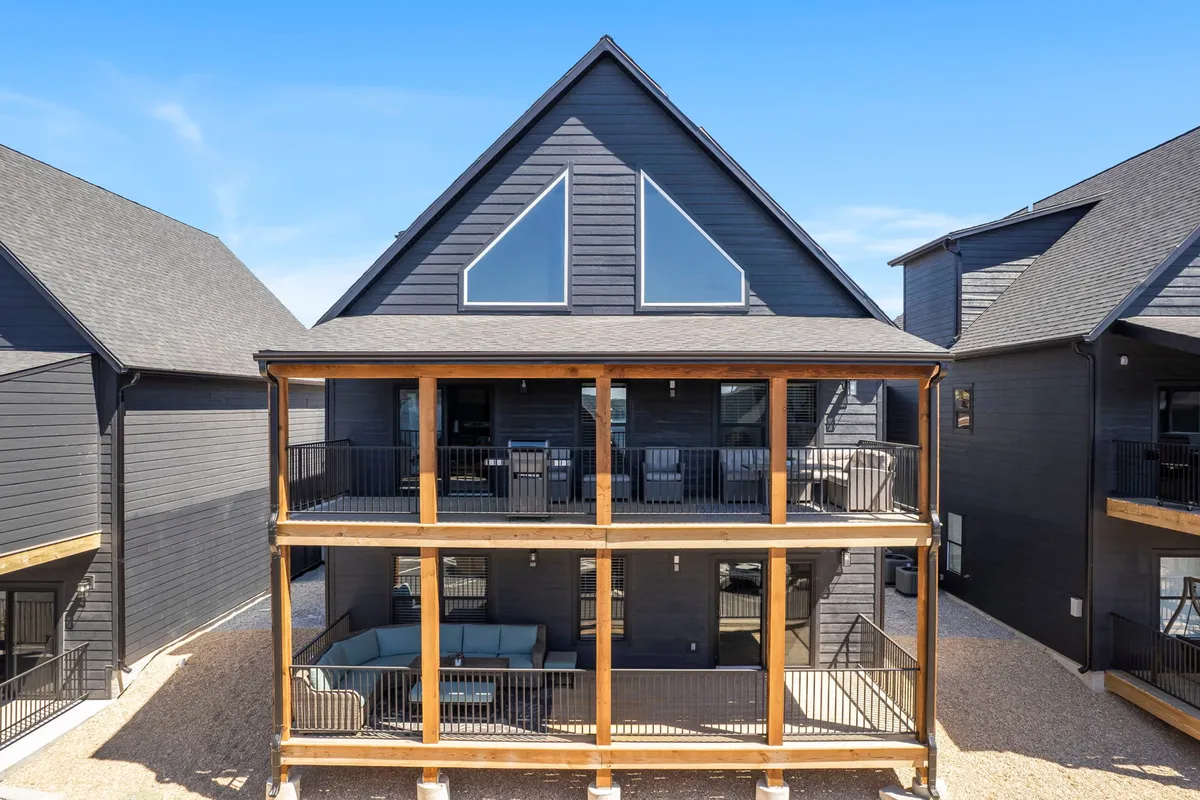 This image features the exterior of the property with a two-story balcony, large triangular windows, wooden beams, and an inviting outdoor seating area. The setting showcases opportunities for relaxing together, enjoying meals al fresco, and taking in the surrounding views with friends or family.