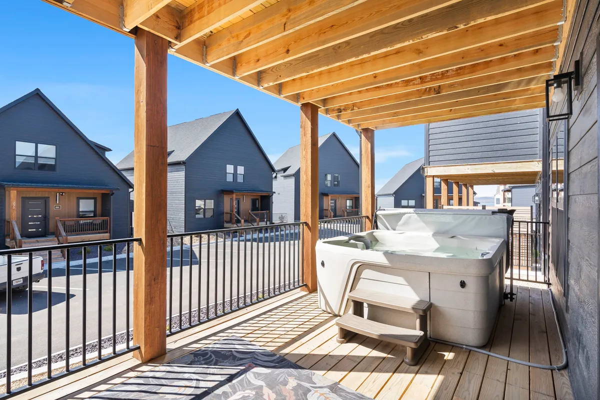 A private hot tub sits on a wooden deck, surrounded by neighboring houses, providing a cozy spot to relax and unwind after a day of activities. The setting hints at evening barbecues or stargazing while soaking in the tub.