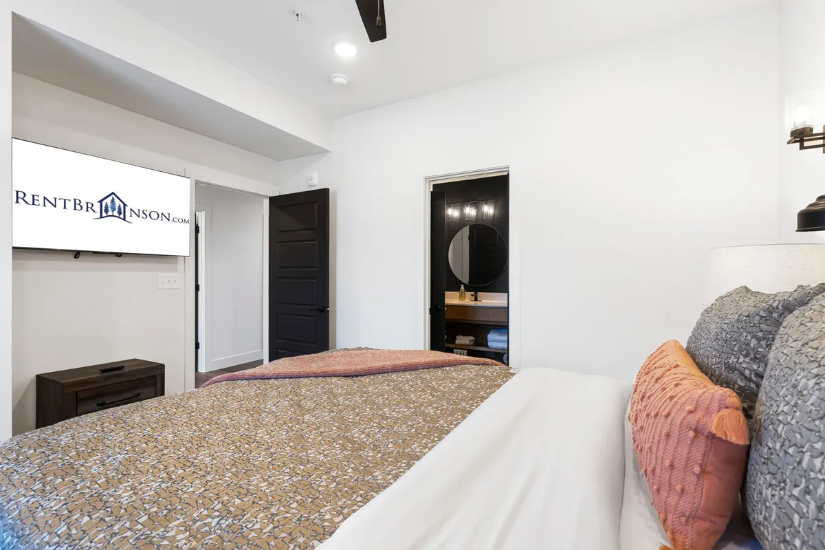 A restful bedroom with a bed adorned with decorative pillows, a television for entertainment, and a doorway leading straight to a stylish ensuite bathroom. The ambiance is both cozy and practical, offering comfort and convenience.