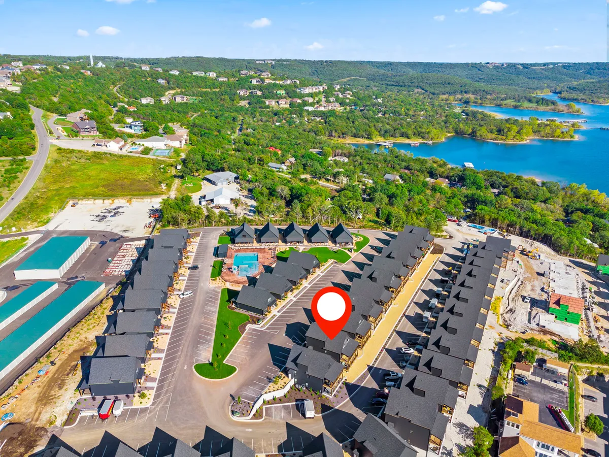 A wide exterior view shows a cluster of houses near a sparkling swimming pool, surrounded by lush greenery and with the lake visible in the background. The communal spaces and pool are ideal for group gatherings, swimming, and socializing.