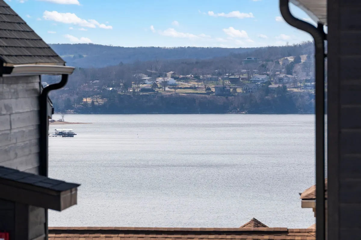 This image features a beautiful view of Table Rock Lake, with rooftops of houses and fluffy clouds above the water. The scene is tranquil and inviting, suggesting possibilities for boating, fishing, or simply enjoying the lakeside ambiance.