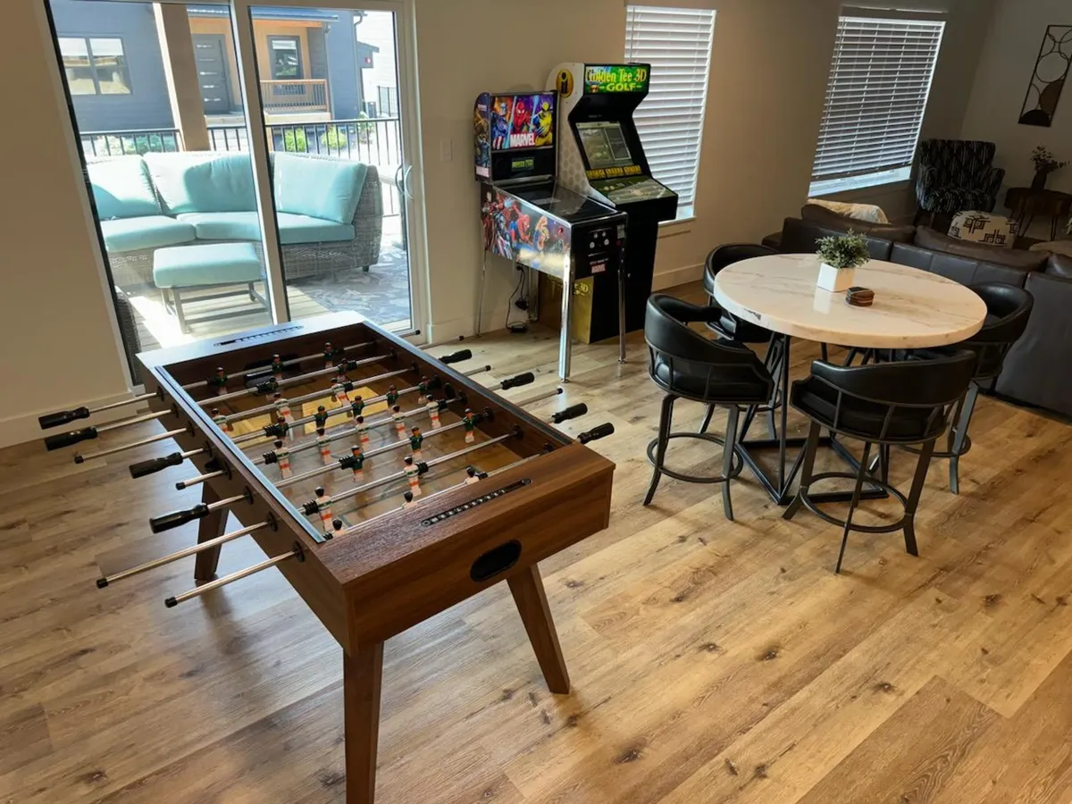 A spacious, playful living area with a foosball table, classic arcade games, a dining table, and a cozy sofa. The layout encourages group activities and relaxation, making it ideal for families, teens, or friend groups seeking fun and connection.