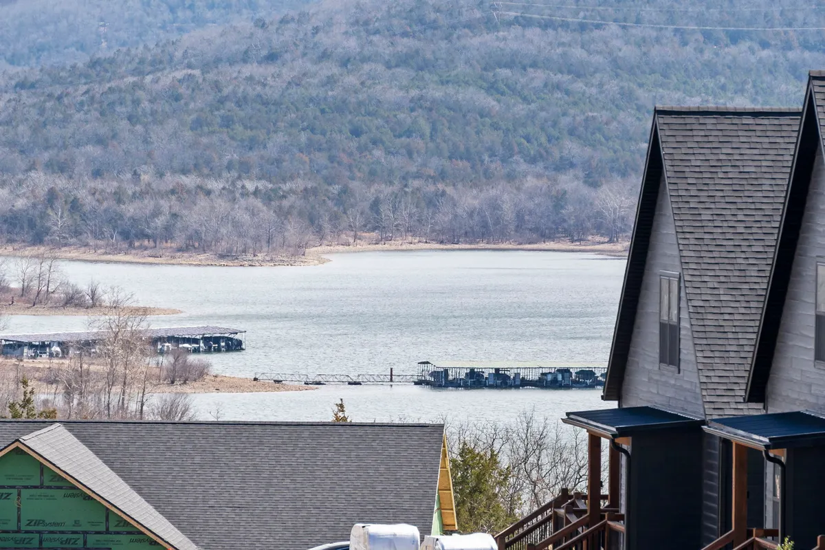 A peaceful vista of a lake with distant mountains and the rooftops of houses in the foreground. The open landscape is ideal for hiking, boating, and leisurely walks, embodying the spirit of outdoor exploration.