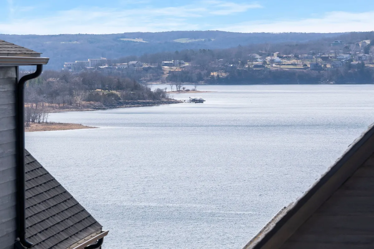 A picturesque view of a calm lake bordered by rolling hills and dotted with houses along the shore. A weathered dock extends over the water, inviting boating, fishing, or lakeside picnics. The scene is bathed in soft, natural light, perfect for highlighting seasonal changes and outdoor adventures.