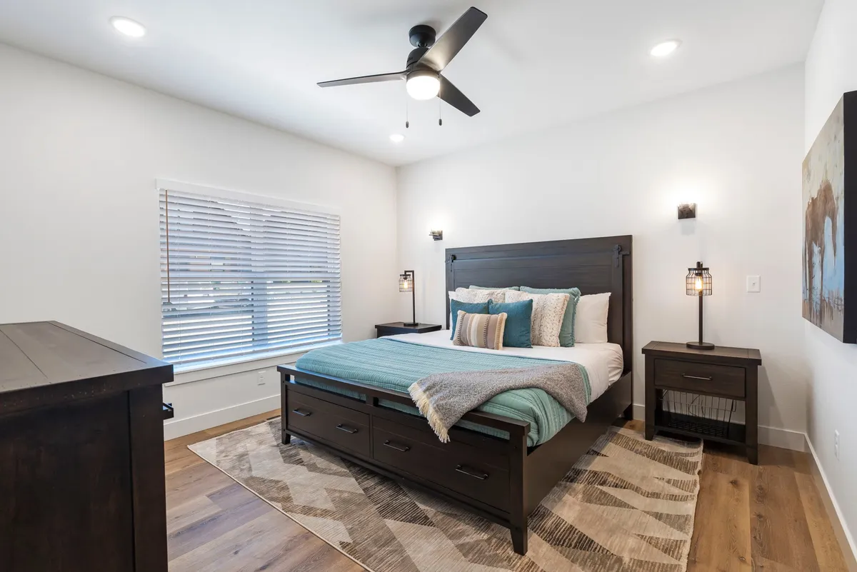 A serene bedroom featuring a plush bed with soft linens, nightstands, a large window allowing in natural light, a cozy rug, and tasteful artwork on the wall. The overall atmosphere is peaceful and inviting, perfect for relaxation and rejuvenation.
