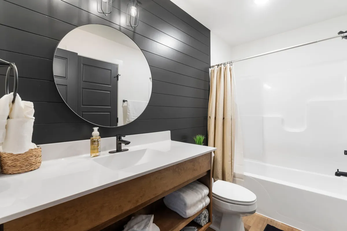 A modern bathroom with a large round mirror, wooden vanity, and inviting white bathtub. The space is bright, clean, and evokes a spa-like feel—ideal for personal relaxation and end-of-day unwinding.